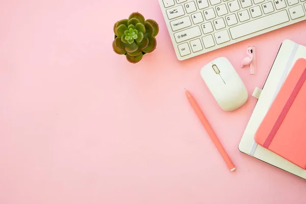 Pink flat lay background. Office desk with keyboard, notebook and pen..