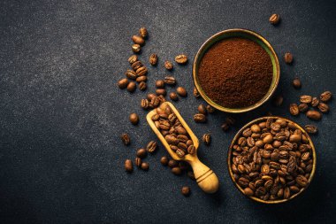 Roasted coffee beans and ground coffee in bowls at dark background. Top view image with copy space.