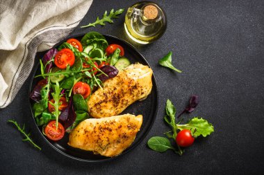 Fresh salad with chicken fillet and vegetables on black kitchen table. Healthy food, keto diet, low carb. Top view with copy space.