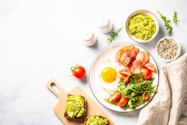Healthy breakfast or lunch. Beacon, eggs, toast with avocado and fresh salad. Top view on white kitchen table.