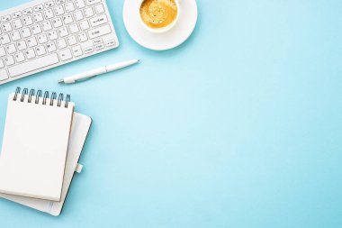 Office table desk with laptop, notepad, pen and cup of coffee. Flat lay on blue with copy space.