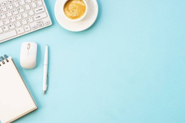 Office table desk with laptop, notepad, pen and cup of coffee. Flat lay on blue with copy space.