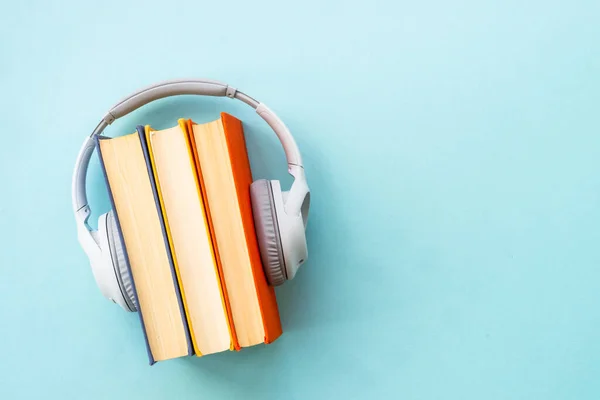 Audio books concept. Headphones and books on blue background. Listen, study, podcast.