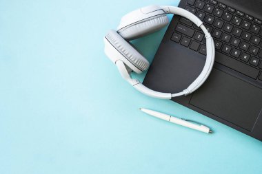 Laptop and wireless headphones on blue background. Flat lay with copy space. Podcast, listening, studying, music concept.