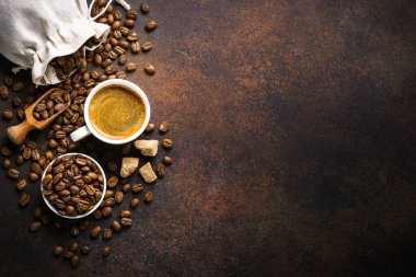 Cup of coffee, roasted coffee beans and sugar at dark table . Top view image with copy space.