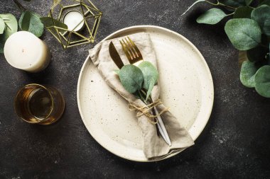 Table setting with white craft plate, cutlery and decorations at black stone table. Top view image.