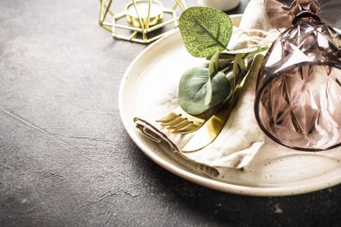 White craft plate, cutlery, napkin, wine glass and eucaliptus at black stone table.