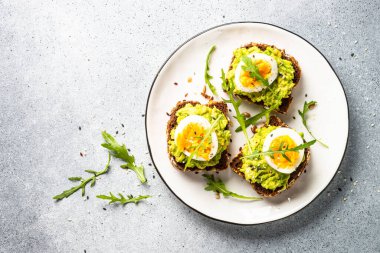 Open sandwich. Whole grain bread with avocado and boiled eggs. Top view on white kitchen table.
