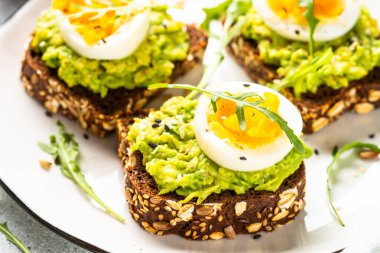 Avocado sandwich. Whole grain bread with avocado and boiled eggs at white plate. Close up image.
