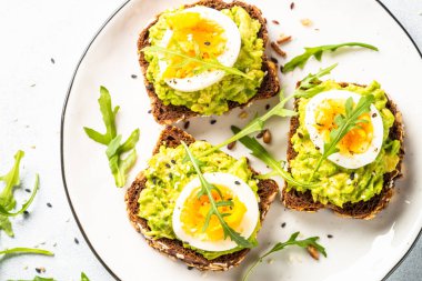 Avocado sandwich. Whole grain bread with avocado and boiled eggs with arugula. Top view on white background.