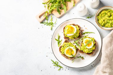 Avocado sandwich. Whole grain bread with avocado and boiled eggs with arugula. Top view on white background.
