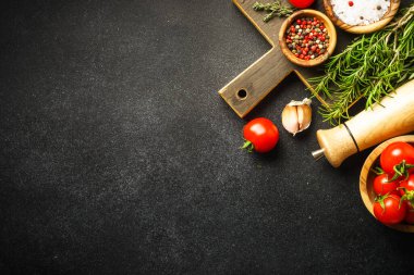 Ingredients for cooking on black stone kitchen table. Herbs, spices and vegetables with wooden cutting board. Flat lay.