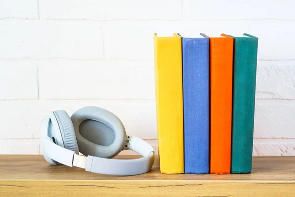 Audio books concept. Wireless Headphones and color books at wooden table white background.