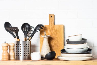 Kitchen table, kitchen utensils, plates, bowls, shakers and wooden cutting board, white modern interior. Modern kitchen interior.