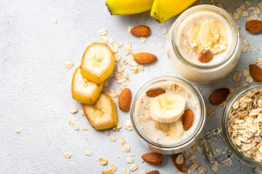 Almond banana smoothie with oat flakes in glass jars at white stone table. Top view.