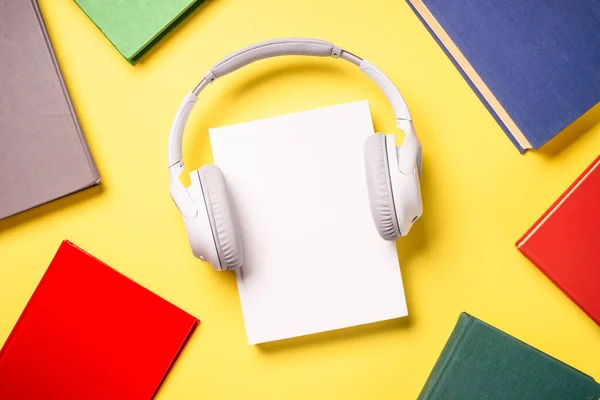 Audio books concept. Headphones and color books at yellow background. Flat lay image with copy space.