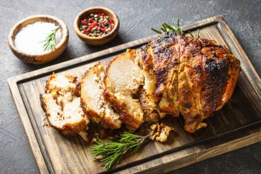 Baked ham sliced on serving board with herbs.