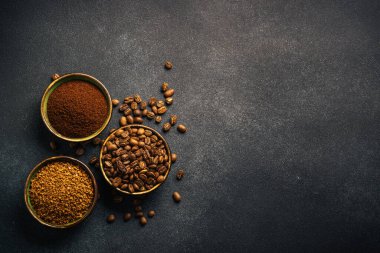 Roasted coffee beans, ground coffee and instant coffee in bowls at dark background. Top view image.