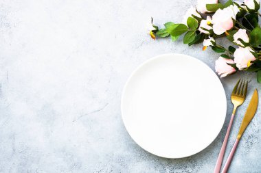 Masa seti beyaz tabak, modern çatal bıçak takımı ve pembe gül çiçekleri. Fotokopi alanı ile bembeyaz yatıyordu.