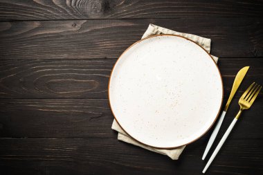 Koyu ahşap masada çatal bıçaklı beyaz tabak. Kopyalama alanı olan en üst görüntü.