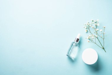Natural cosmetic products at blue background. Cream, serum and white flowers. Flat lay image with copy space.