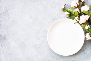 Beyaz tabak ve çiçekli bahar masası. Kopyalama alanı olan beyaz arkaplanda üst görünüm.