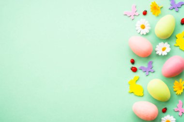 Paskalya geçmişi. Yumurta, tavşan, bahar çiçekleri ve kelebek. Yeşil arkaplanda düz yatış modeli.