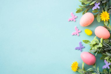 Mavi üzerine bahar ya da Paskalya arkaplanı. Yumurtalar, bahar yaprakları, çiçekler ve renkli kelebekler. Kopyalama alanı olan düz.