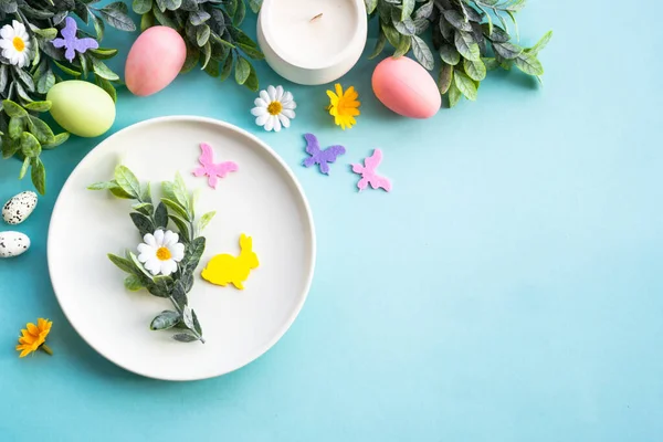 Easter food background. White plate with eggs, spring flowers, green leaves and butterflies. Flat lay.