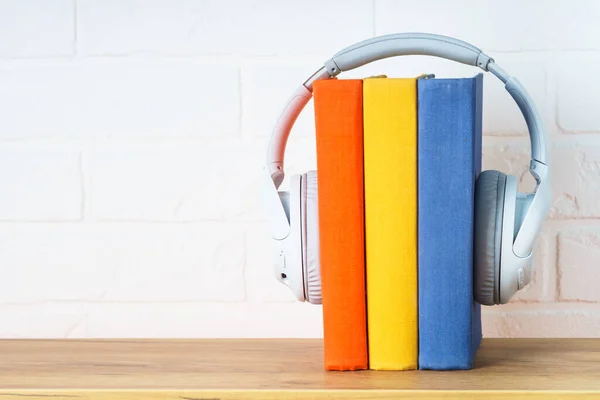 Audio books concept. Wireless Headphones and color books at woden table.