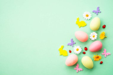 Paskalya geçmişi. Yumurta, tavşan, bahar çiçekleri ve kelebek. Yeşil arkaplanda düz yatış modeli.