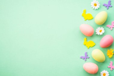 Paskalya geçmişi. Yumurta, tavşan, bahar çiçekleri ve kelebek. Yeşil arkaplanda düz yatış modeli.