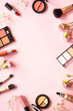 Makeup professional cosmetics on pink background with flowers. Flat lay with copy space.