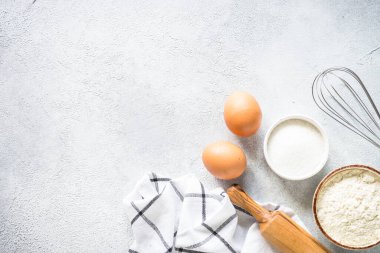 Arkaplan malzemeleri pişiriyorum. Un, şeker, yumurta ve diğer şeyler hafif taş masada. Kopyalama alanı olan üst görünüm.