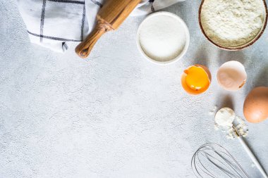 Arkaplan malzemeleri pişiriyorum. Un, şeker, yumurta ve diğer şeyler hafif taş masada. Kopyalama alanı olan üst görünüm.