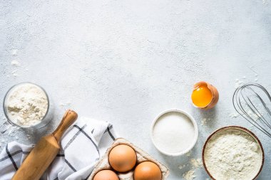 Arkaplan malzemeleri pişiriyorum. Un, şeker, yumurta ve diğer şeyler hafif taş masada. Kopyalama alanı olan üst görünüm.