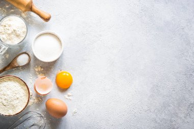 Flour, sugar, eggs and rolling pin at light stone table. Top view with copy space.