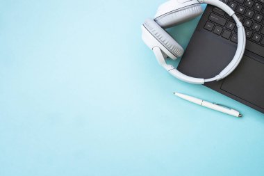 Laptop and wireless headphones on blue background. Flat lay with copy space. Podcast, listening, studying, music concept.