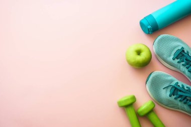 Spor, sağlıklı yaşam tarzı konsepti. Spor ayakkabılar, dambıllar, yeşil elma ve bir şişe su. Kopyalama alanı olan düz.