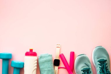 Pembe arka planda spor aletleri, düz bir görüntü. Spor ayakkabıları, dambıllar, havlu ve bir şişe su. Eğitim, egzersiz ve spor konsepti.