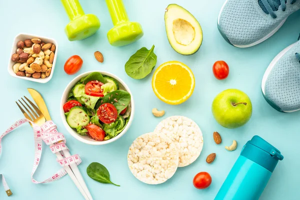 Diet food, healthy lifestyle and fitness background. Vegan salad, crispbread, fruits and dumbell. Flat lay with copy space.