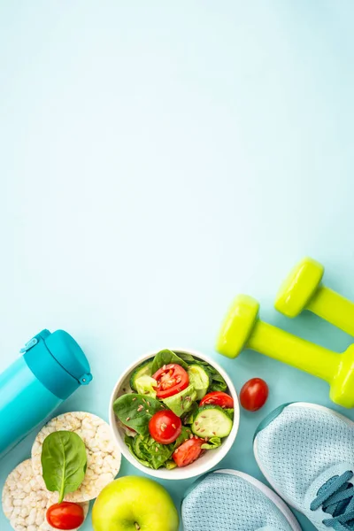 Healthy lifestyle and diet food background. Sport shoes, dumbell and healthy food on blue. Flat lay with copy space.