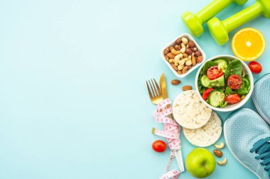 Sağlıklı bir yaşam tarzı ve kilo verme geçmişi. Spor ayakkabılar, dambıl ve mavi üzerine sağlıklı yiyecekler. Kopyalama alanı olan düz.