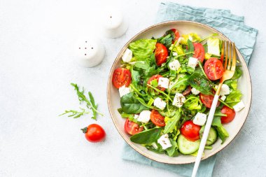 Ispanaklı yeşil salata, roka, domates ve zeytinyağlı feta. Beyaz üzerine üst görünüm.