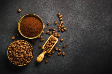 Roasted coffee beans and ground coffee in bowls at dark background. Top view image with copy space.