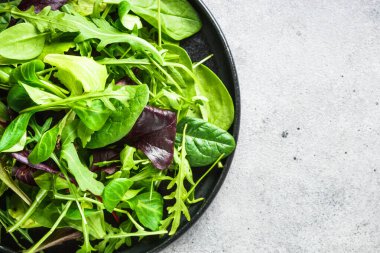 Green salad with fresh leaves assortment in black plate. Top view, close up.