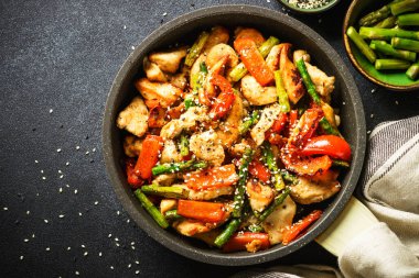 Chicken stir fry with vegetables at stone background. Top view with copy space.
