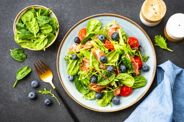 Taze jambonlu yeşil salata, yeşil yapraklar ve domatesler koyu masada. Düz yatıyordu.