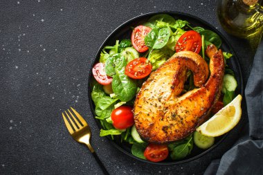 Somon bifteği ve siyah arka planda taze yeşil salata. Keto diyeti, sağlıklı yiyecekler. Üst görünüm kopyalama alanı.