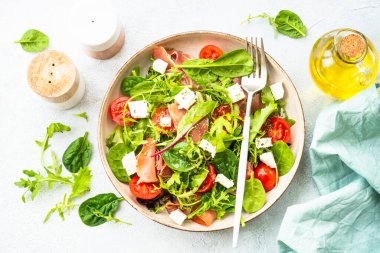 Yeşil yapraklı, domatesli ve jamonlu sağlıklı salata. Sanatsal tabakta üst görünüm.
